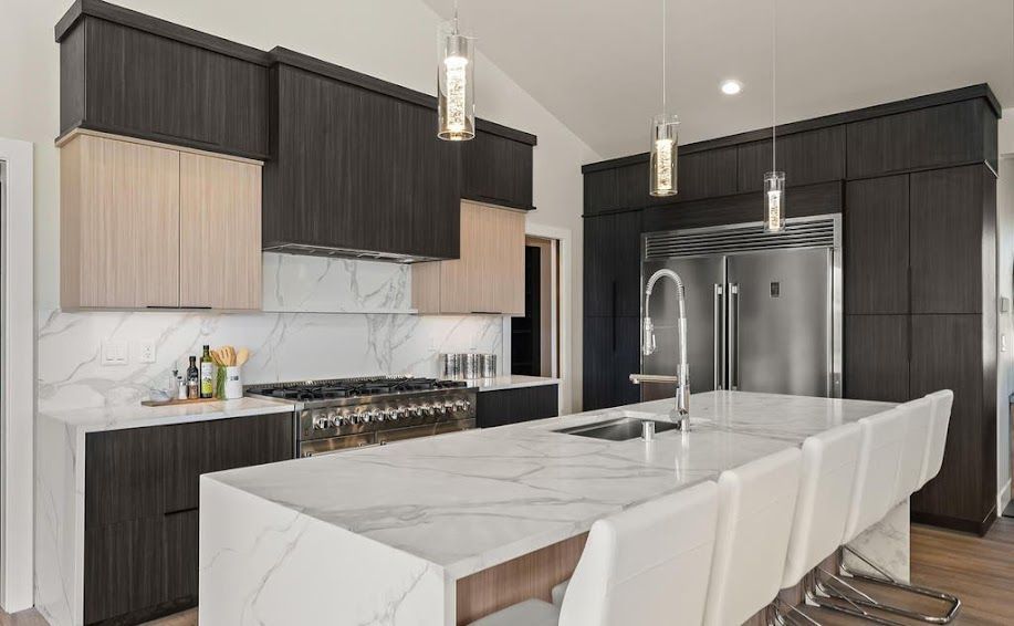 Modern kitchen with marble countertops, dark and light cabinets, island with seating, stainless steel appliances.