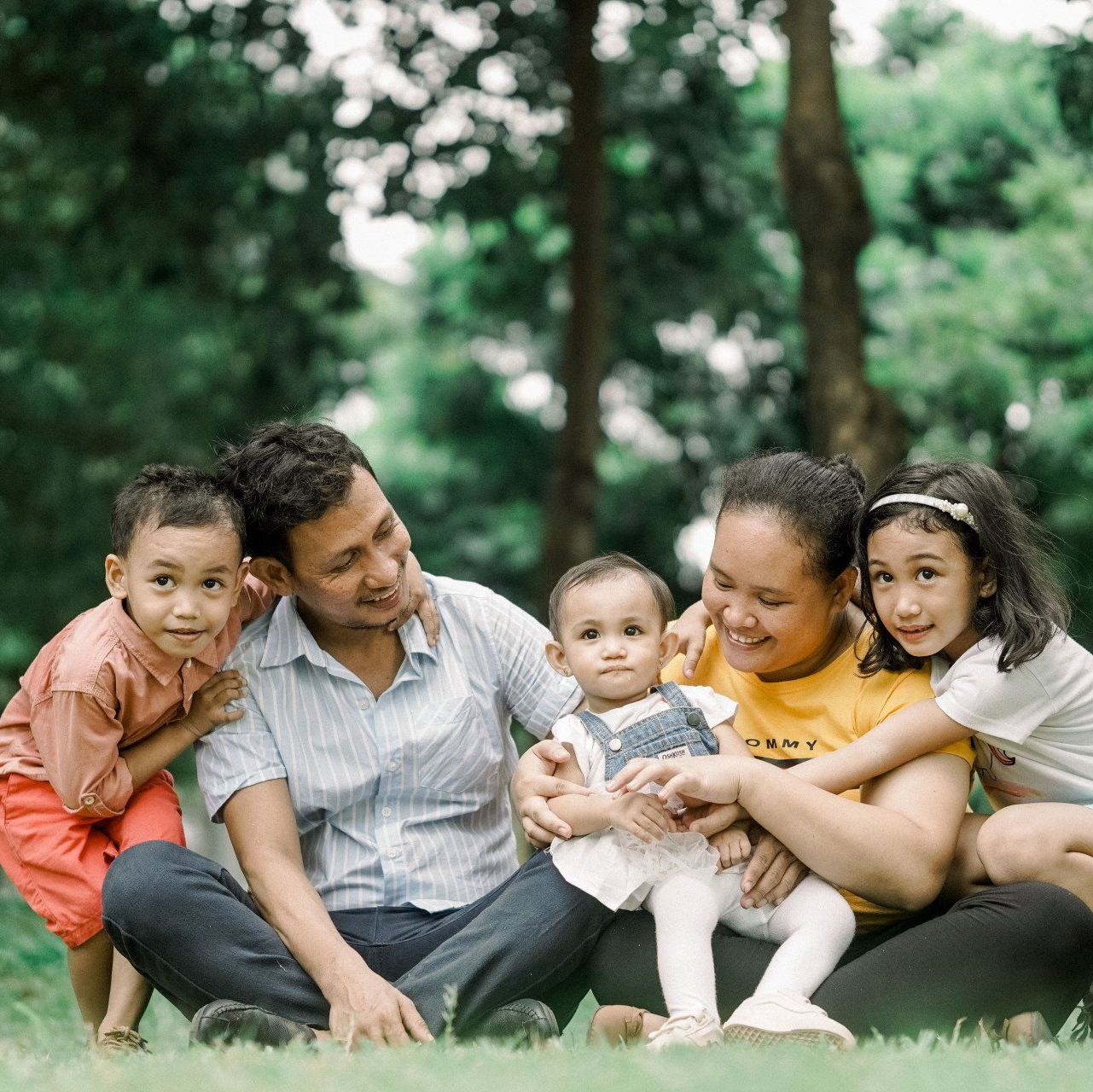 Una familia de cinco personas sentada junta en el césped de un parque, sonriendo a la cámara.