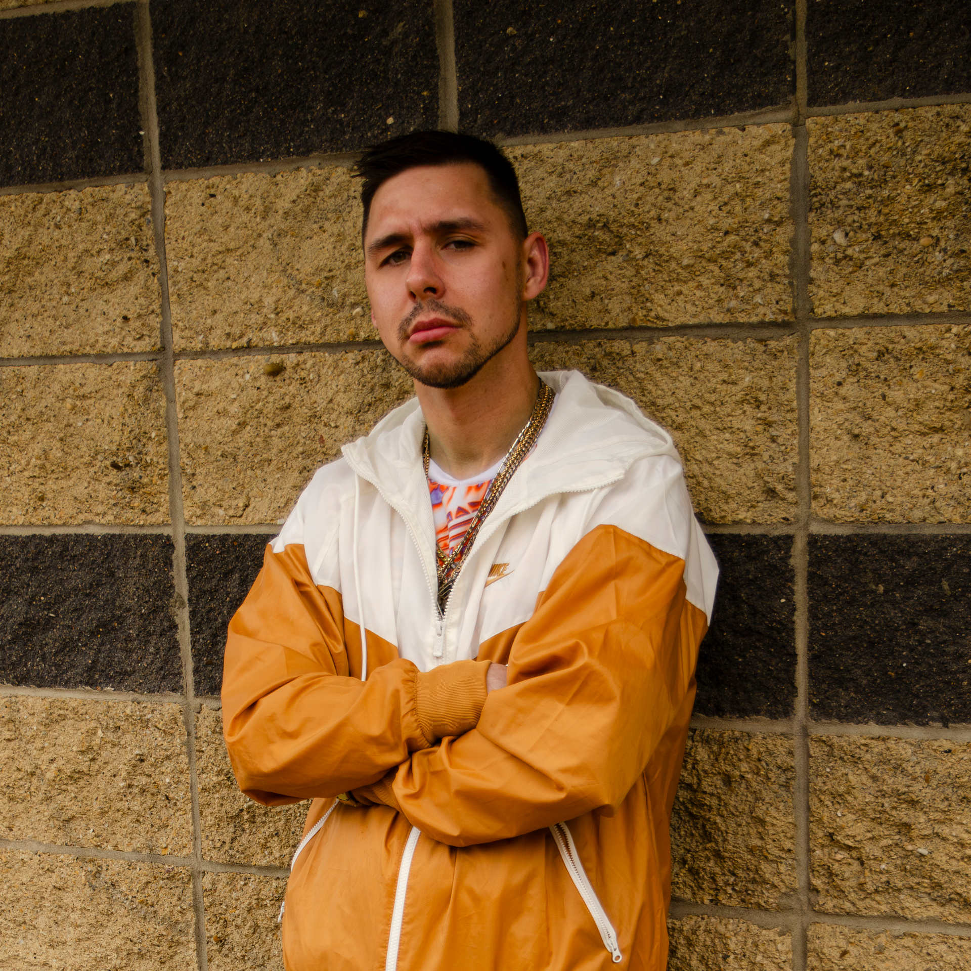 A stern looking man with olive complexion & a caramel & white coloured windbreaker