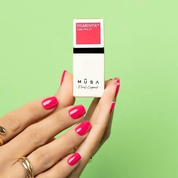 Donna che tiene in mano un rossetto rosa e mostra lo smalto abbinato su uno sfondo verde.