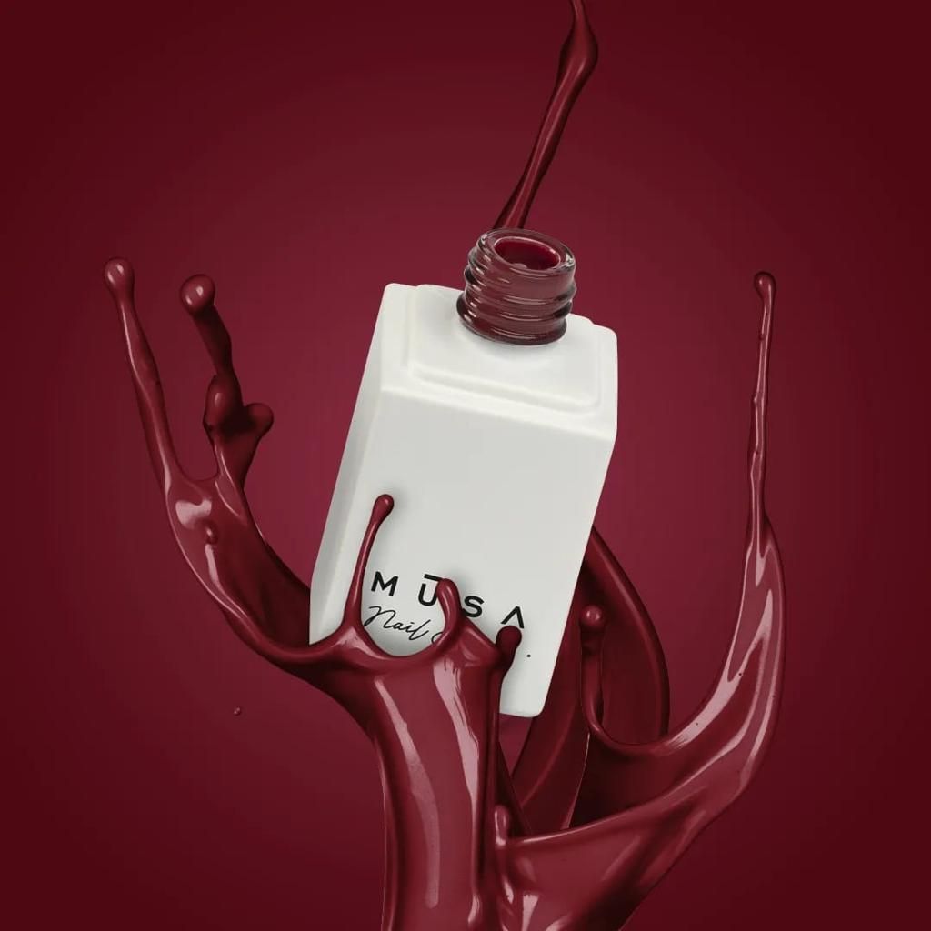 Flacone bianco di profumo con schizzi di liquido rosso scuro su sfondo rosso scuro.
