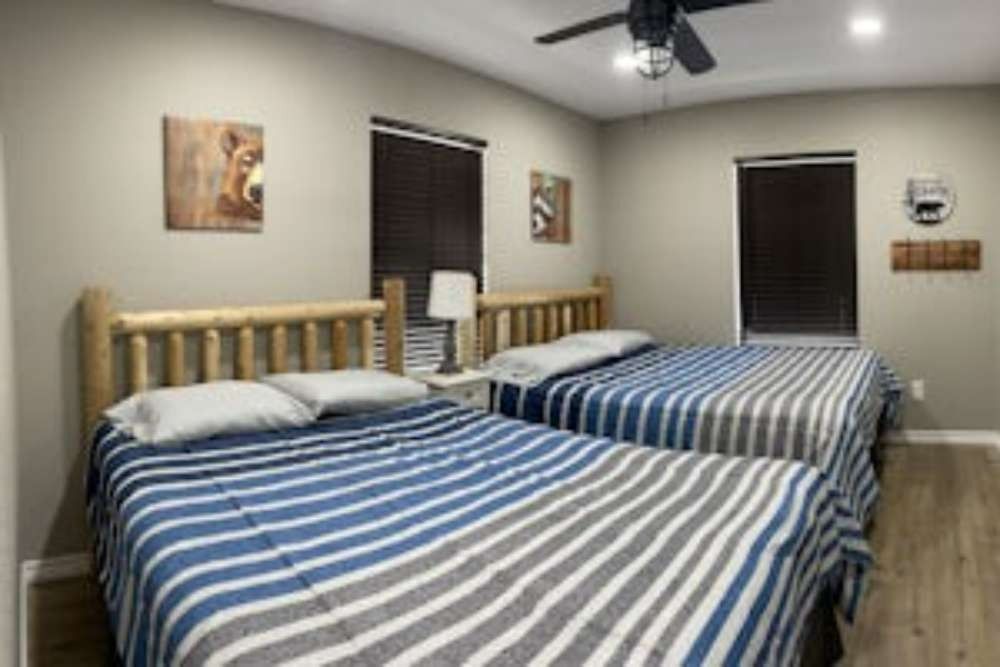 Two double beds with blue striped bedding in a room with wood trim, matching window shades, and rustic decor.