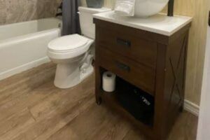 A bathroom with a wooden vanity, toilet, and bathtub. The floor is tiled with wood-look planks.
