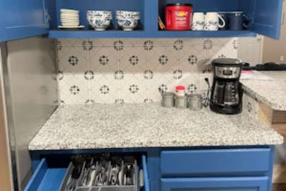 Blue kitchen cabinets with a granite countertop and decorative backsplash. A drawer is open, revealing silverware.