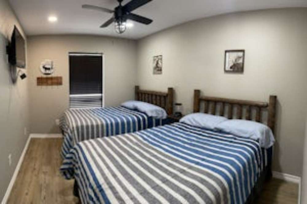 Two beds in a bedroom with blue and gray striped blankets, rustic wooden headboards, and a ceiling fan.