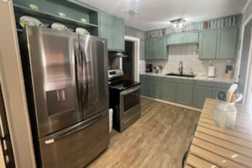 A kitchen with sage green cabinets and stainless steel appliances. The flooring is a light wood grain.