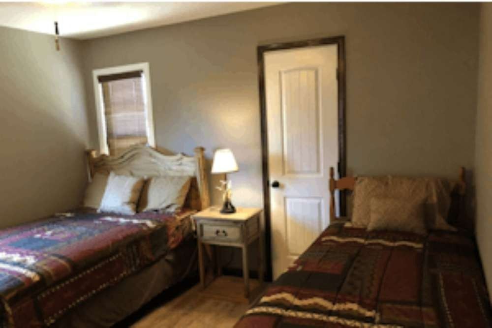 Two beds in a room with a nightstand and lamp between them. The walls are gray.
