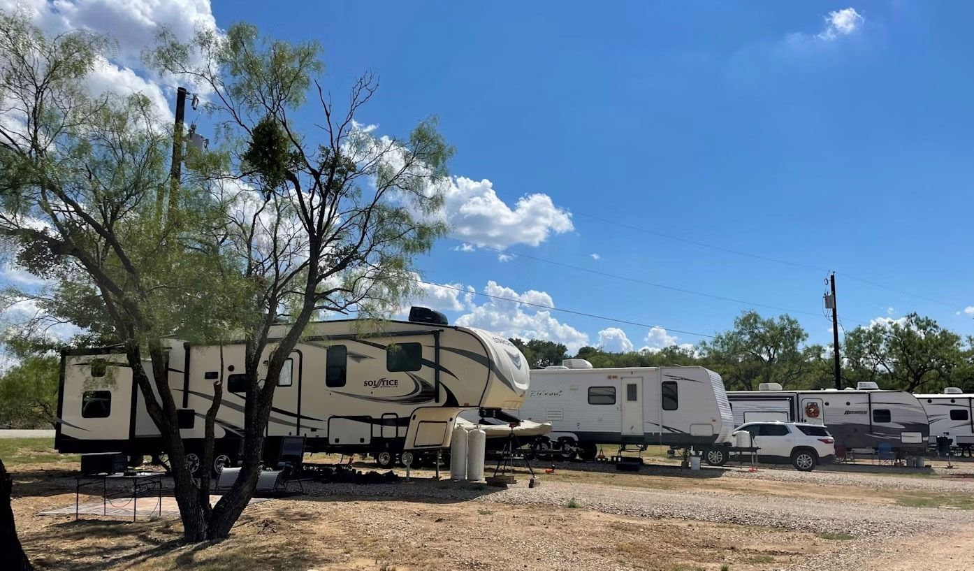 RVs parked at a campsite on a sunny day with blue skies and some trees.