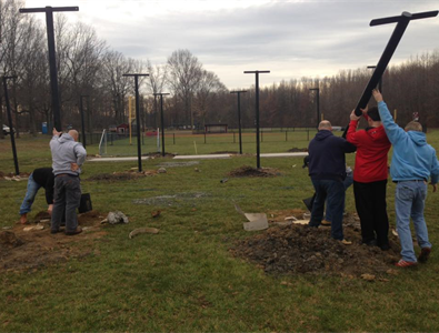 Volunteers lifting black posts into the ground at a park on a cloudy day