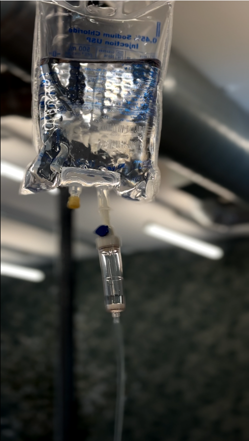 Clear IV bag with blue fluid hanging in a medical setting, with tubing and drip chamber visible