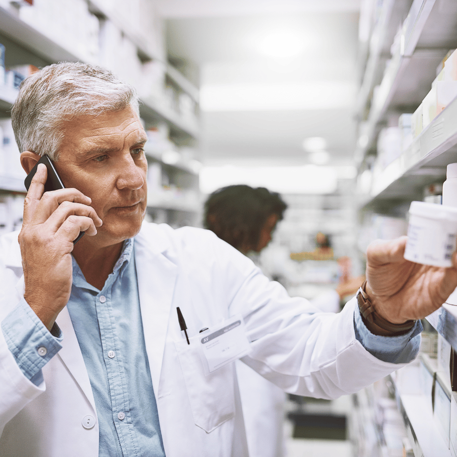 Pharmacist in white coat checking medicine stock in a pharmacy aisle
