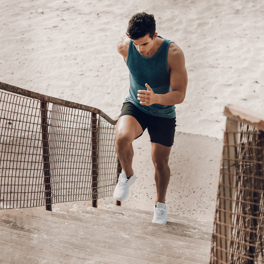 Man running up a sandy stairway, wearing a teal tank top, black shorts, and white shoes.