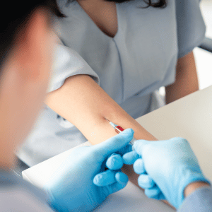 Gloved clinician drawing blood from a patient’s arm at a medical appointment