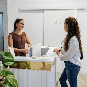 Two women talking at a reception desk in a bright office or clinic