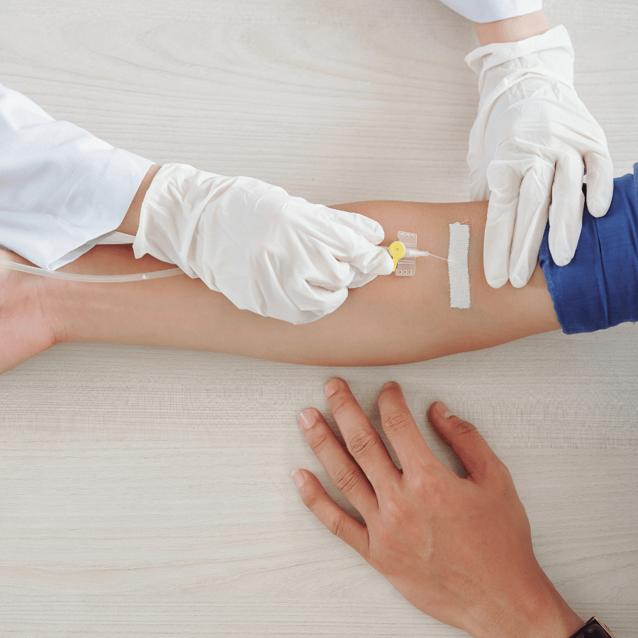 Gloved nurse inserting IV into a patient’s arm on a clinic bed