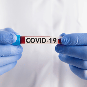 Gloved hands holding a COVID-19 test tube labeled “COVID-19”