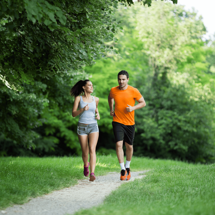 Two runners in orange and gray jogging on a green park path