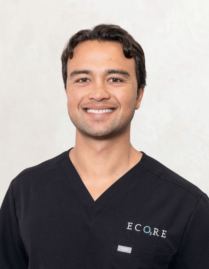 Smiling person in black scrub top with ECORE logo against a plain light background