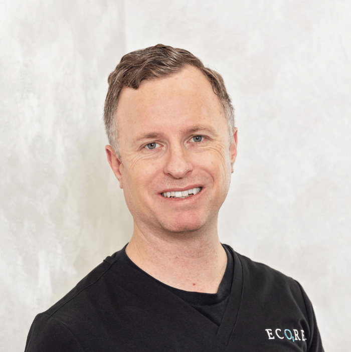 Smiling person in a black shirt with ECCO logo, standing against a light background