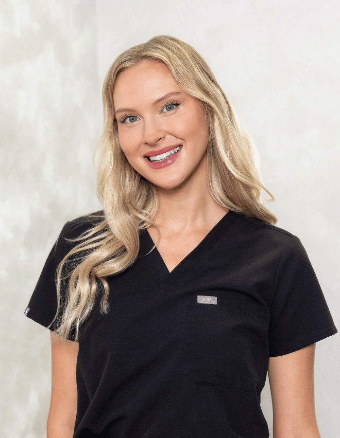 Smiling blonde woman in black scrub top against a light background