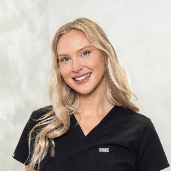 Smiling blonde woman in black scrub top against a light background