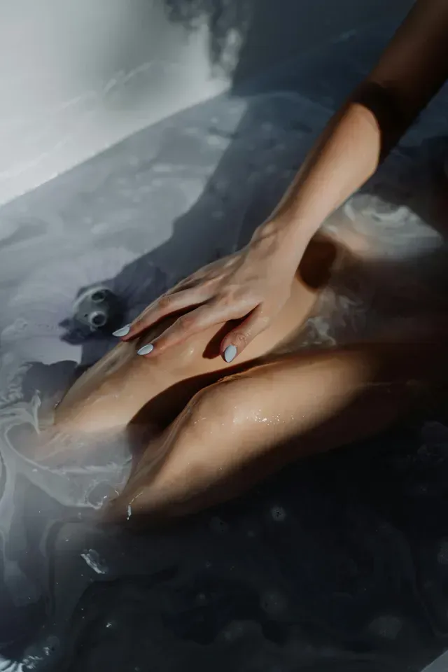 Person resting in a bath, with a hand on their stomach and water softly reflecting light.