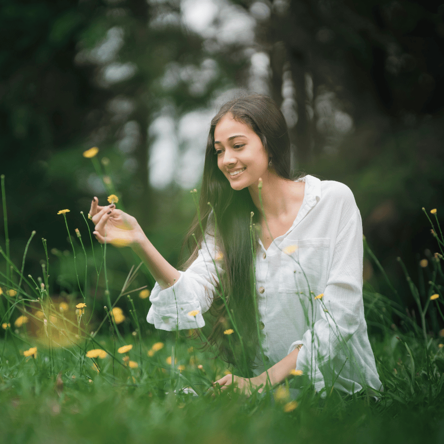 Woman smiling in a green field, gently touching wildflowers in soft natural light