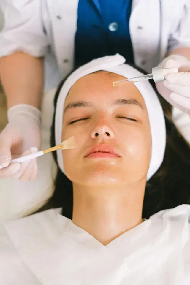 Facial treatment in progress as a clinician applies serum to a relaxed client with a headband.