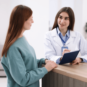 Patient speaking with a doctor at a clinic reception desk, doctor holding a clipboard and smiling