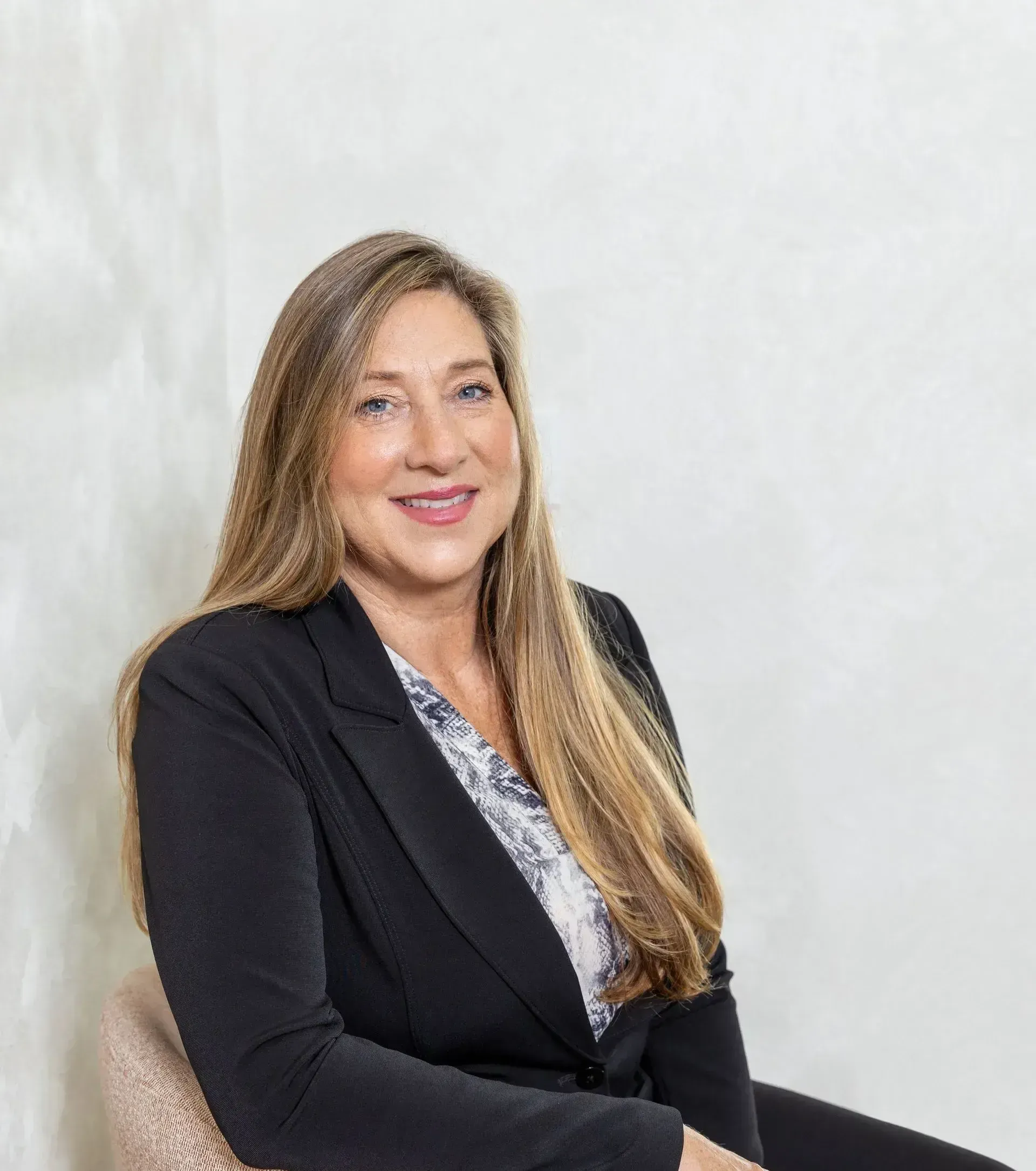 Portrait of a smiling woman in a black blazer seated against a light background