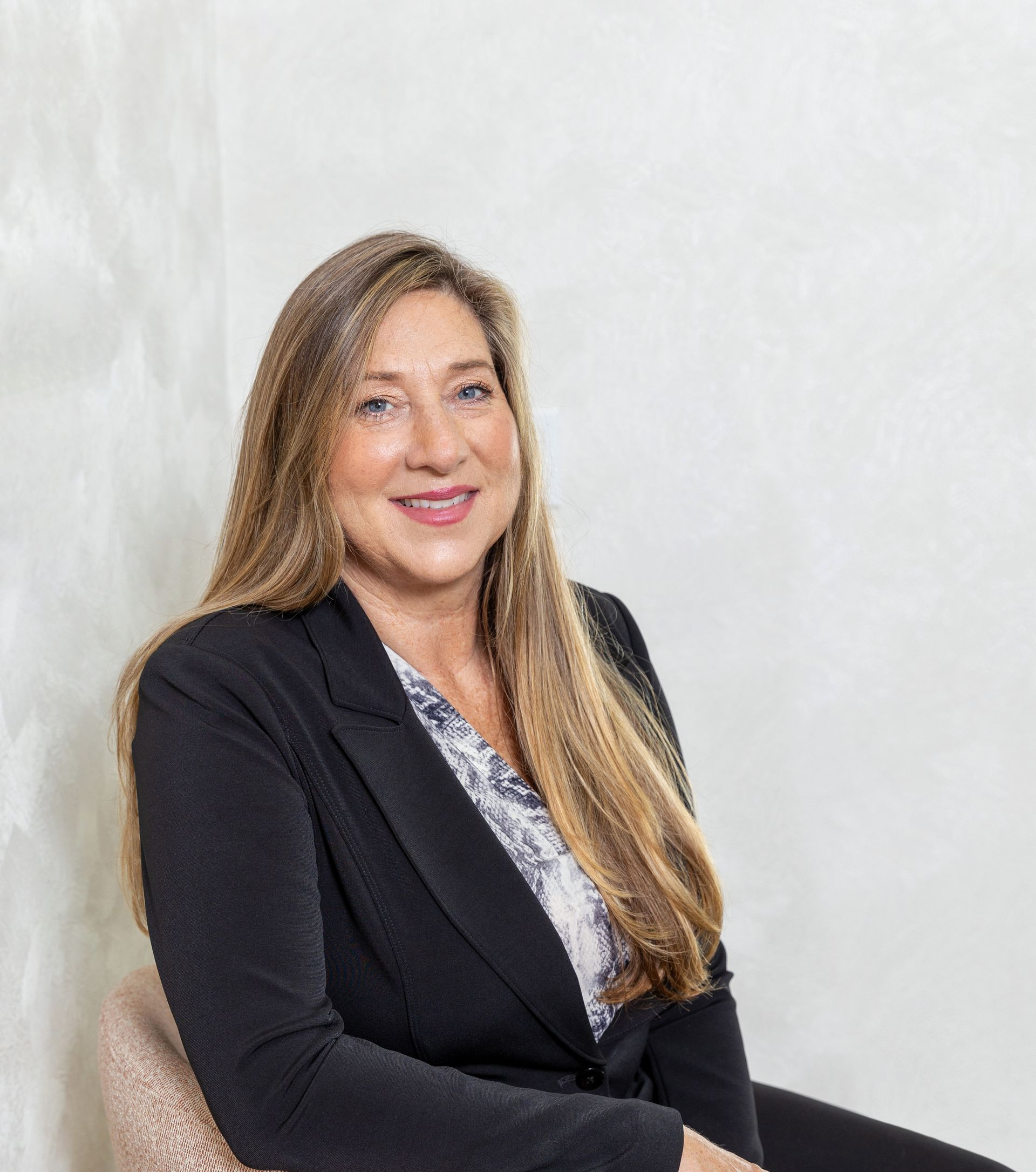 Portrait of a smiling woman in a black blazer seated against a light background