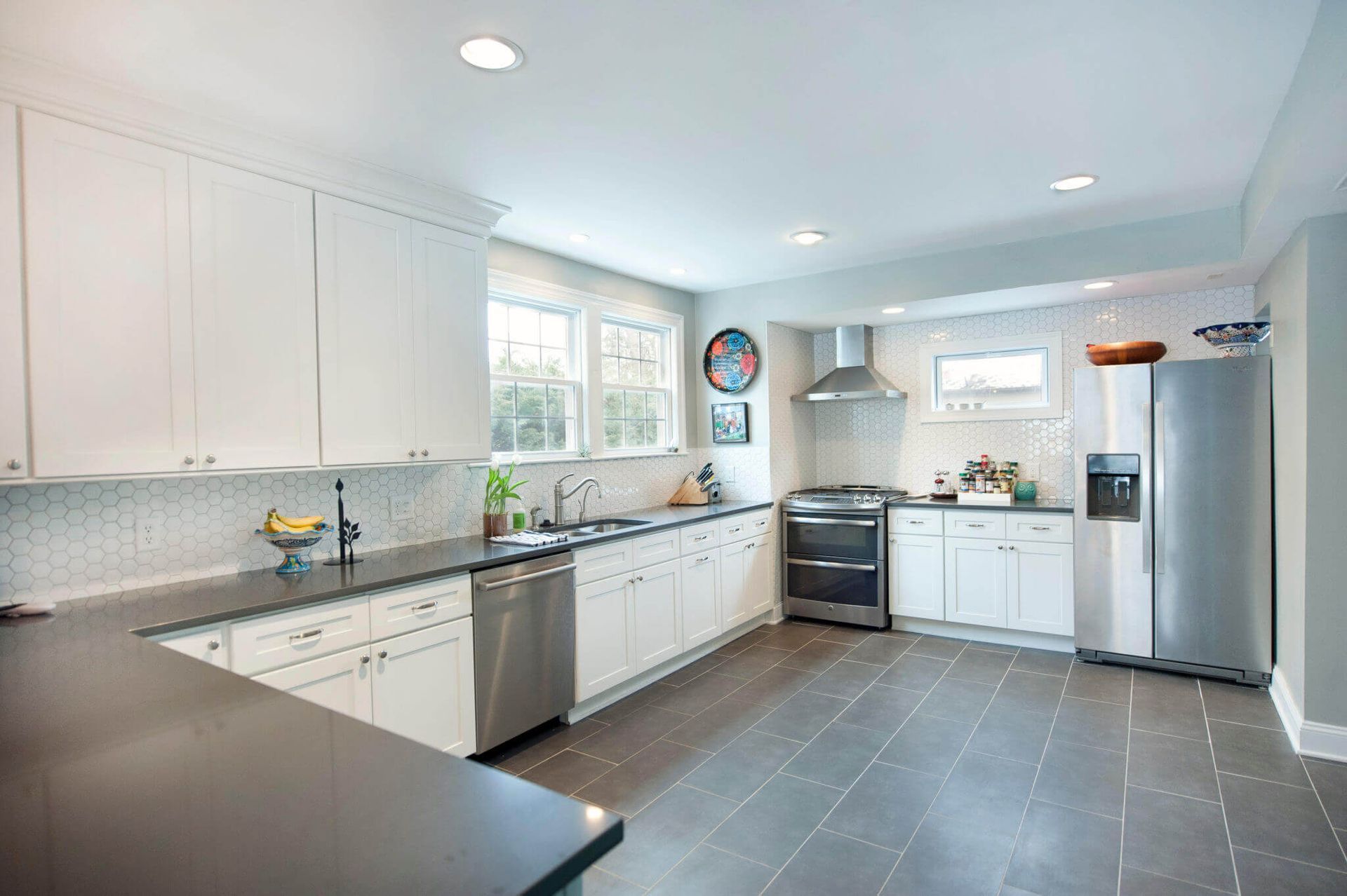 Modern kitchen with white cabinets, stainless appliances, gray tile floor, and bright windows