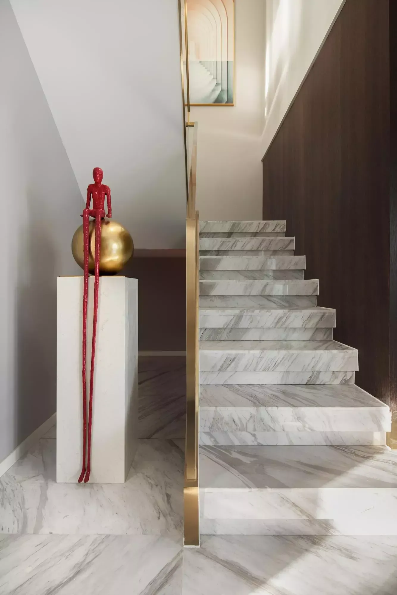 Escadaria de mármore com corrimão dourado, escultura de uma figura vermelha sobre uma esfera dourada.