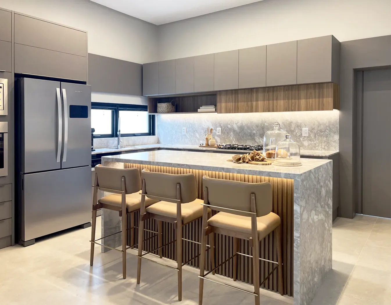 Cozinha moderna com armários cinza, eletrodomésticos de aço inoxidável e uma ilha de mármore com banquetas.