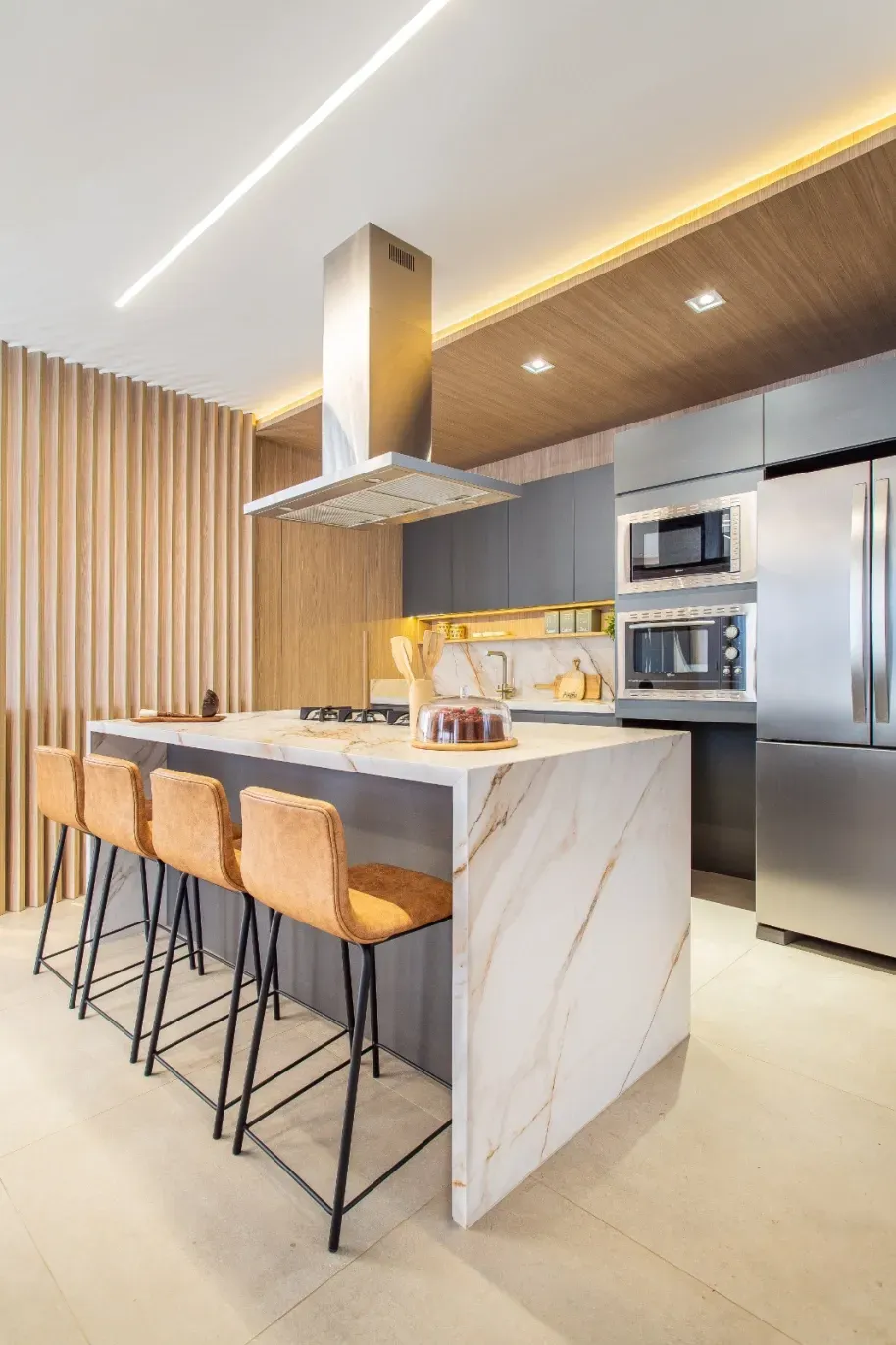 Cozinha moderna com ilha de mármore, banquetas, eletrodomésticos de aço inoxidável e detalhes em madeira.