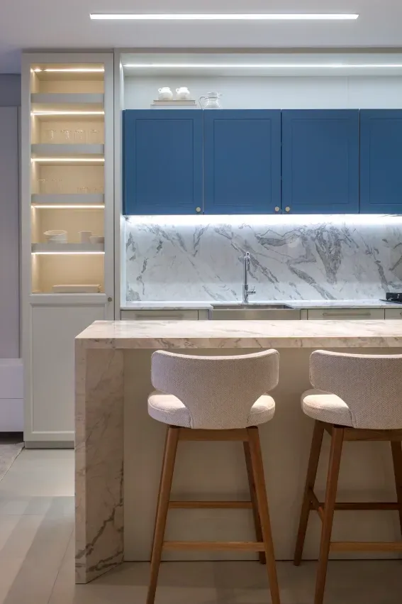 Cozinha moderna com armários azuis, backsplash de mármore e uma ilha em tom claro com dois bancos.