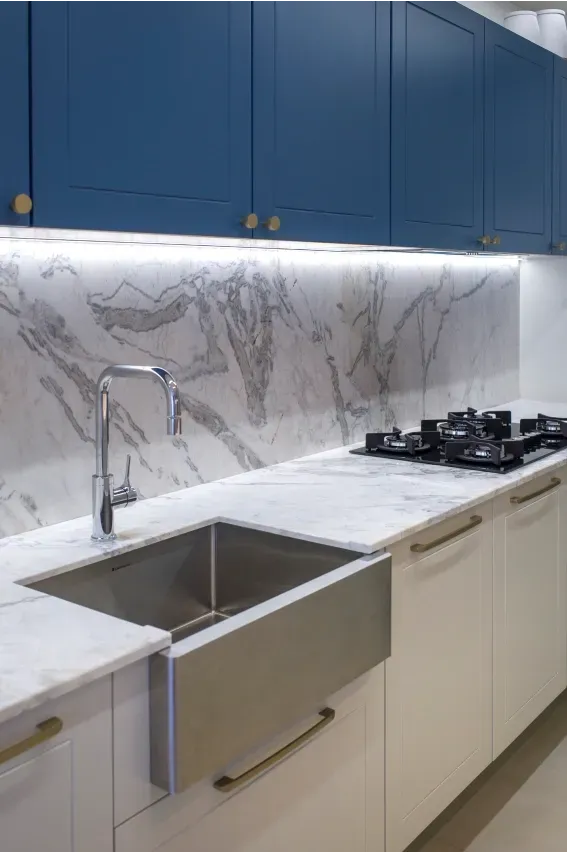 Cozinha moderna com armários superiores azuis, backsplash de mármore, pia de aço inoxidável e armários inferiores brancos.