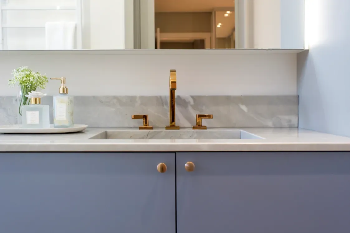 Móvel de banheiro azul com bancada de mármore, torneira dourada e paredes azul-claras.