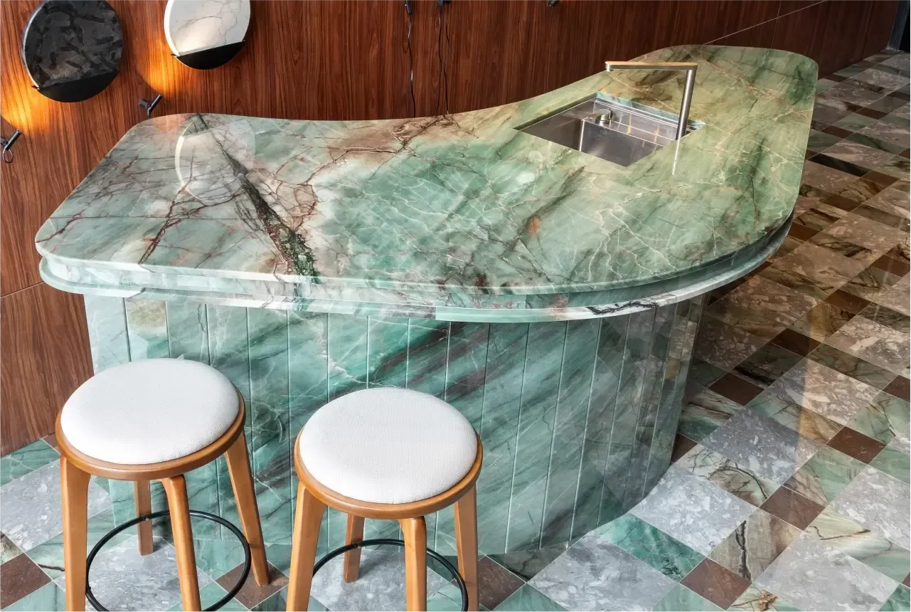Bar de mármore verde com banquetas em uma sala com azulejos do mesmo estilo.