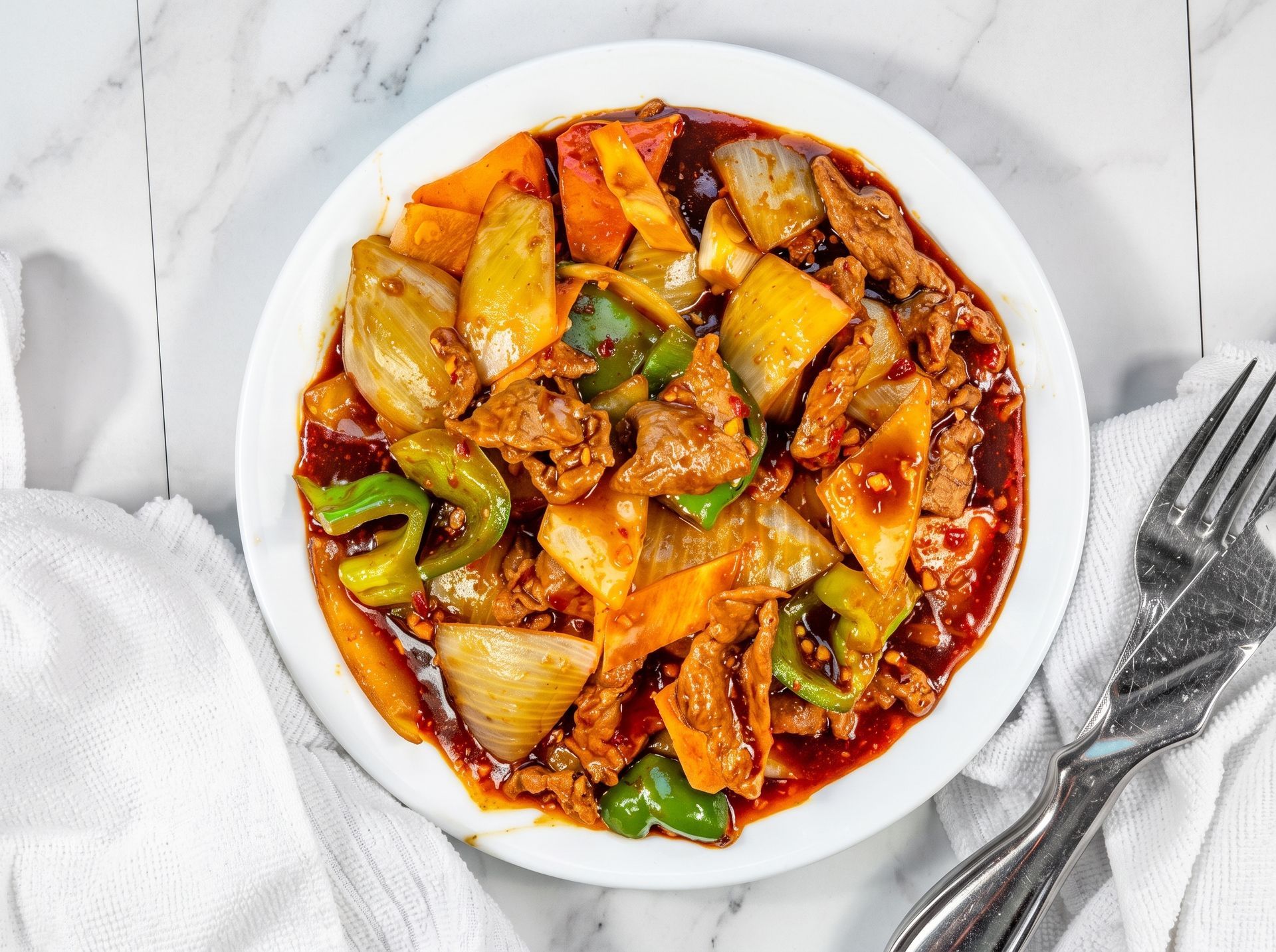 Bowl of saucy stir-fried vegetables on a white marble table with a fork and napkin nearby