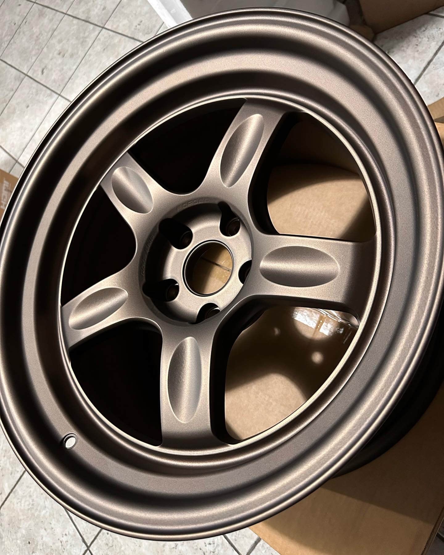 Bronze five-spoke car wheel rim in a cardboard box