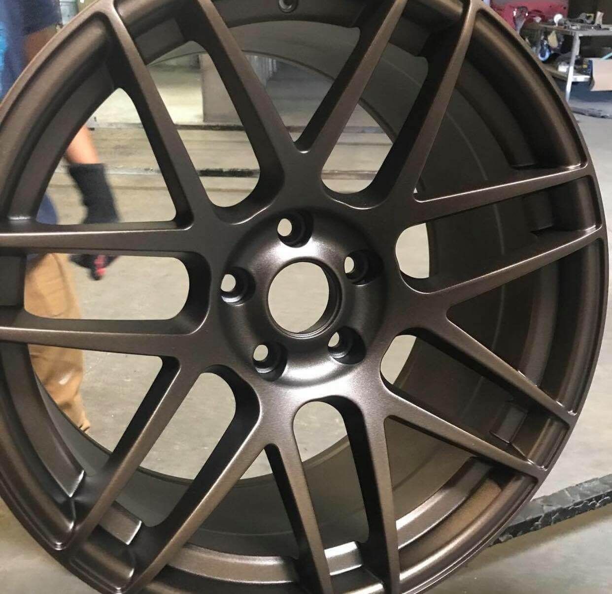 Black multi-spoke car alloy wheel rim in a workshop setting