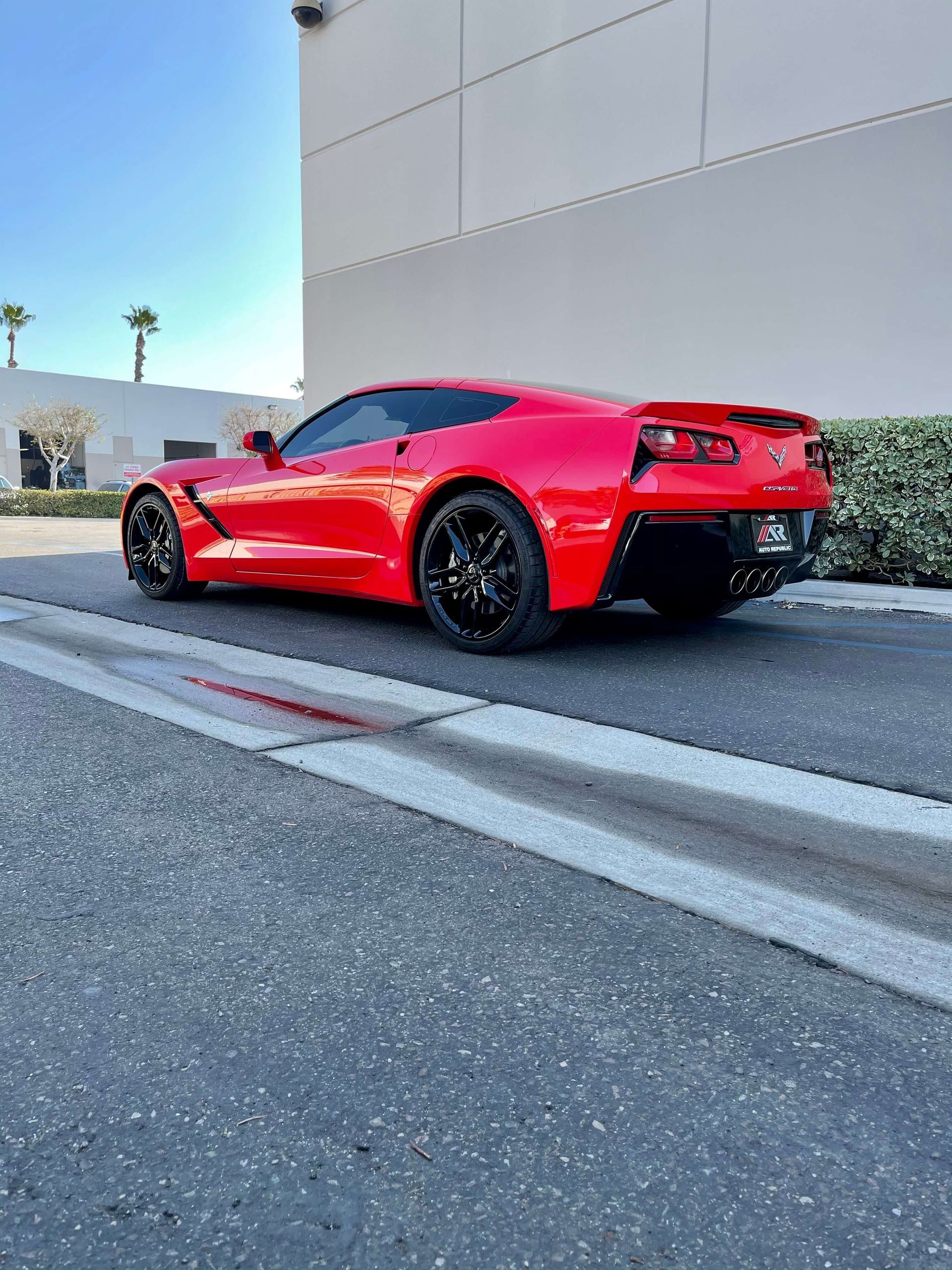 Red sports car parked by a curb beside a white building on a sunny street.