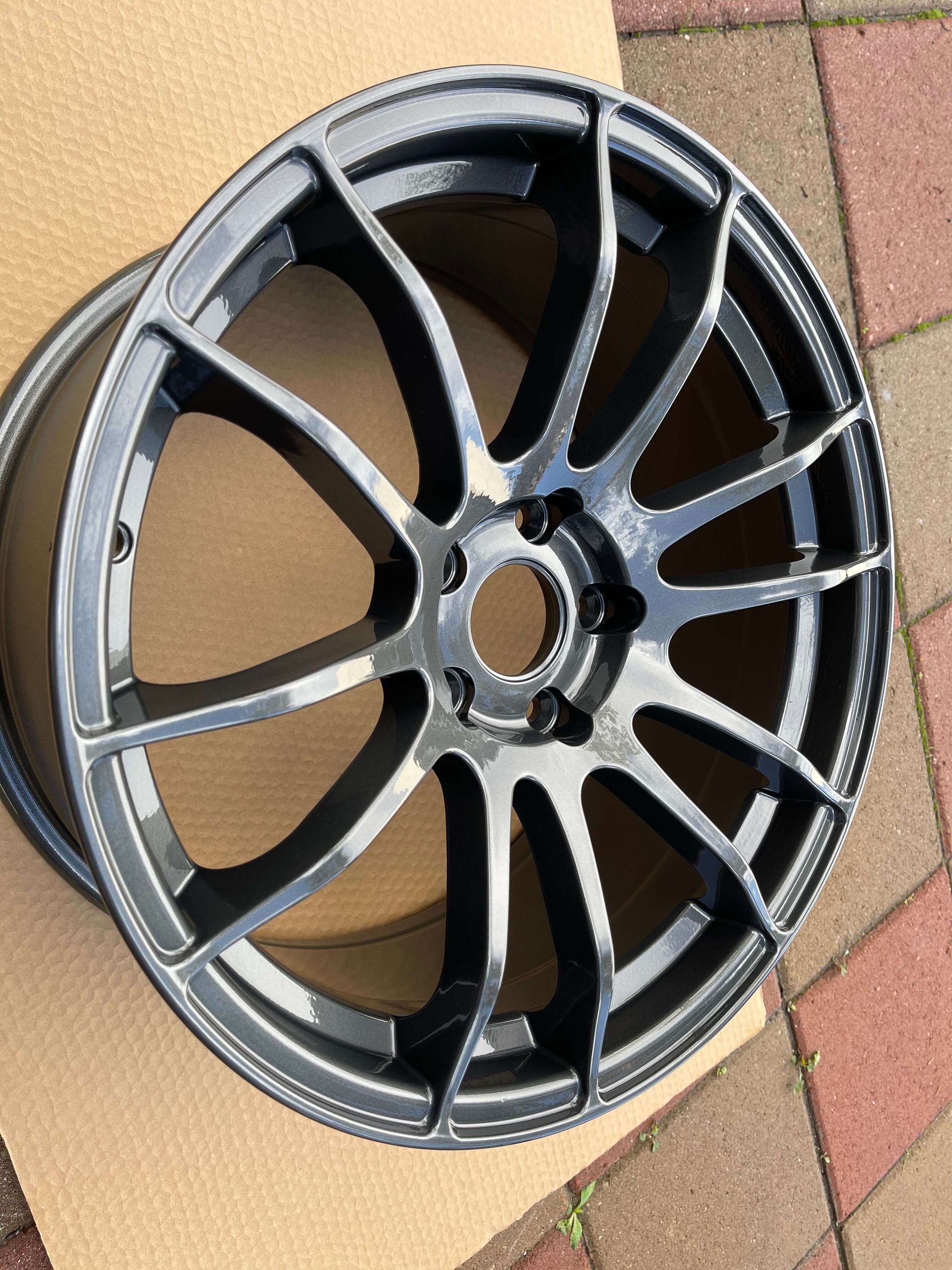 Black alloy car wheel rim leaning on a tiled floor outdoors.