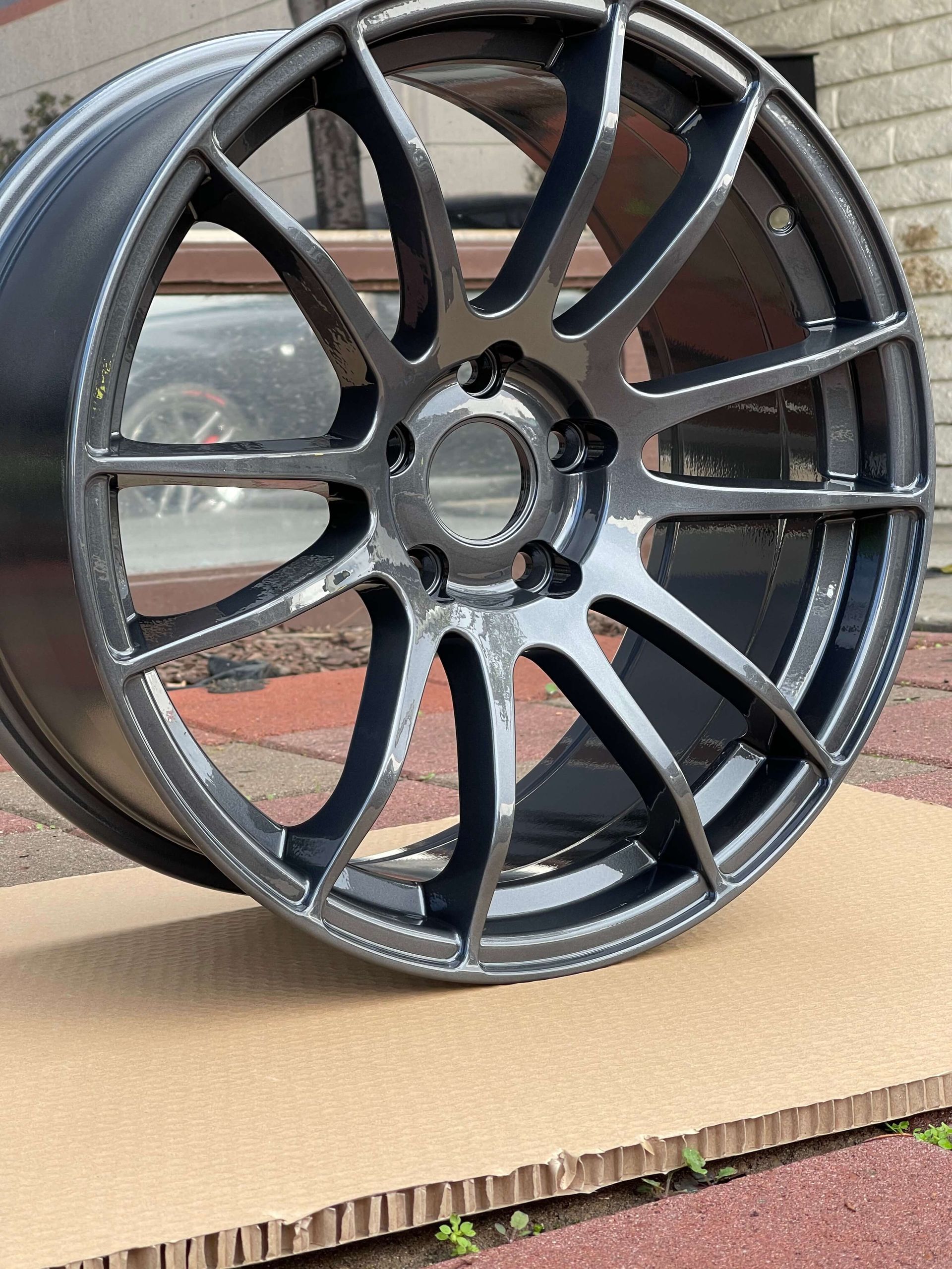 Glossy black multi-spoke alloy wheel rim leaning on cardboard outdoors