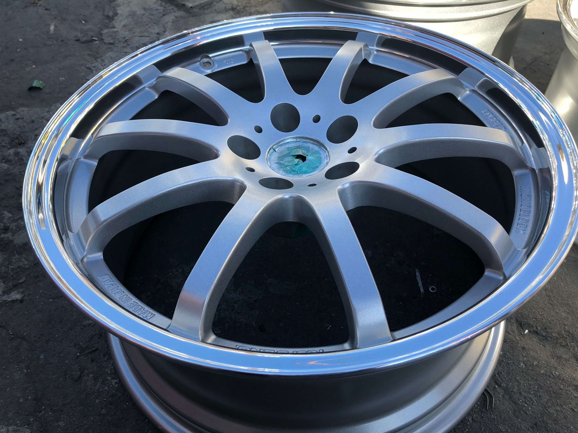 Chrome multi-spoke car wheel rim with a blue center hub on a reflective surface