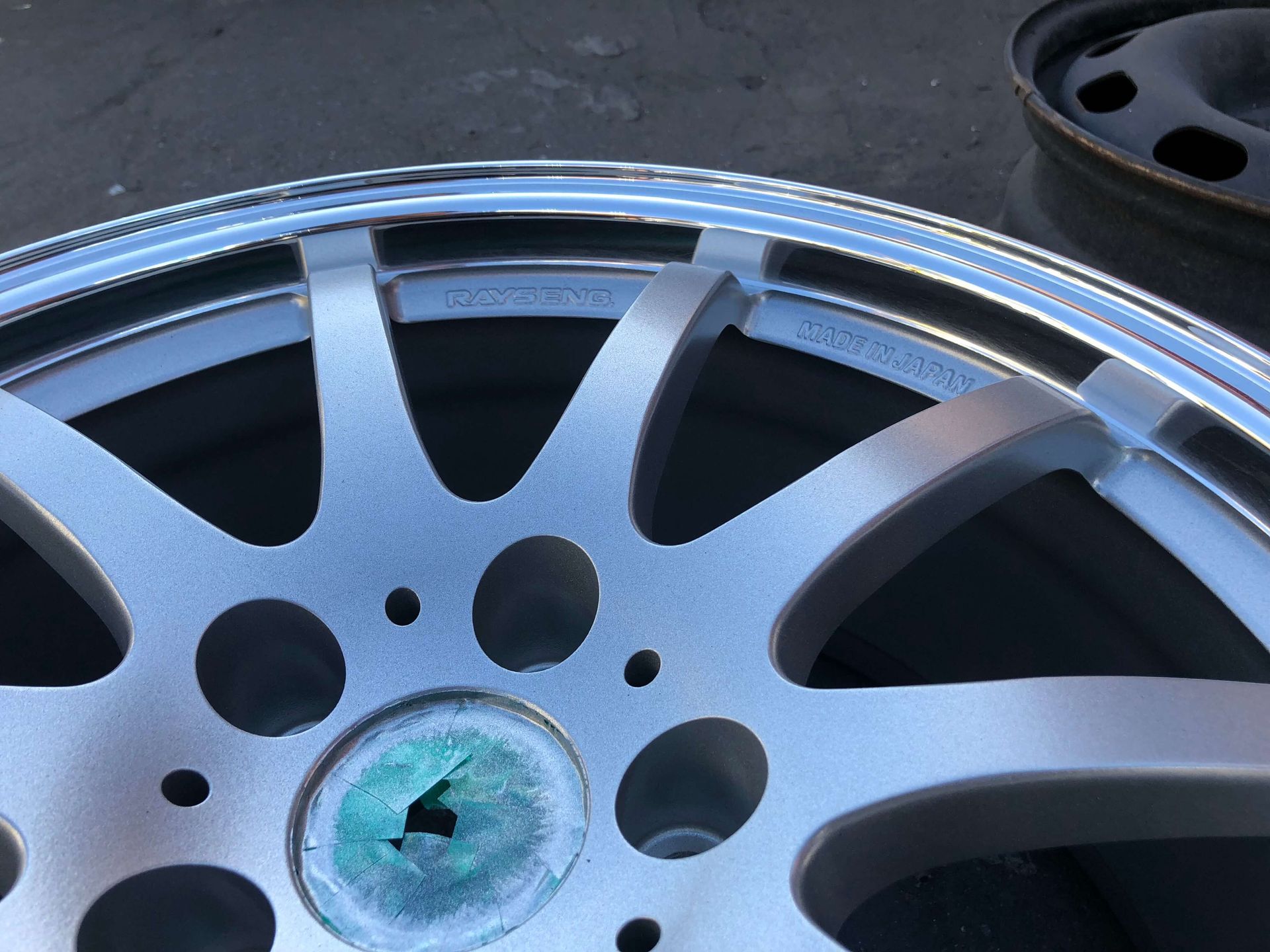 Close-up of a silver alloy wheel rim with multiple spokes, resting on a dark surface.