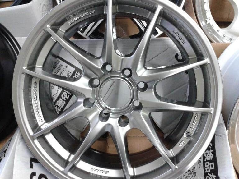 Silver multi-spoke alloy car wheel rim displayed indoors, with tire mounted on a shelf behind it