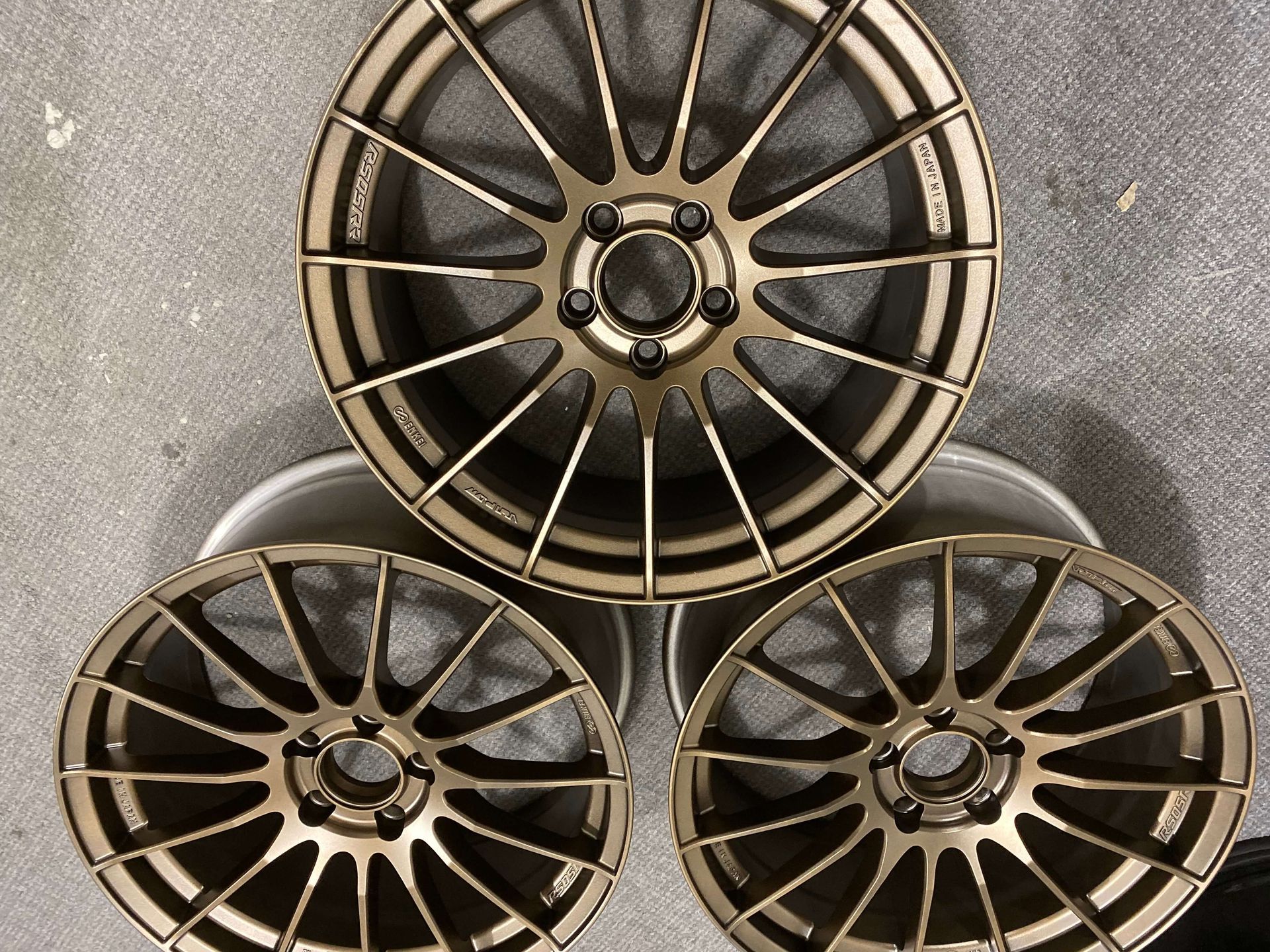 Three bronze and black alloy car rims on concrete, arranged in a triangle.
