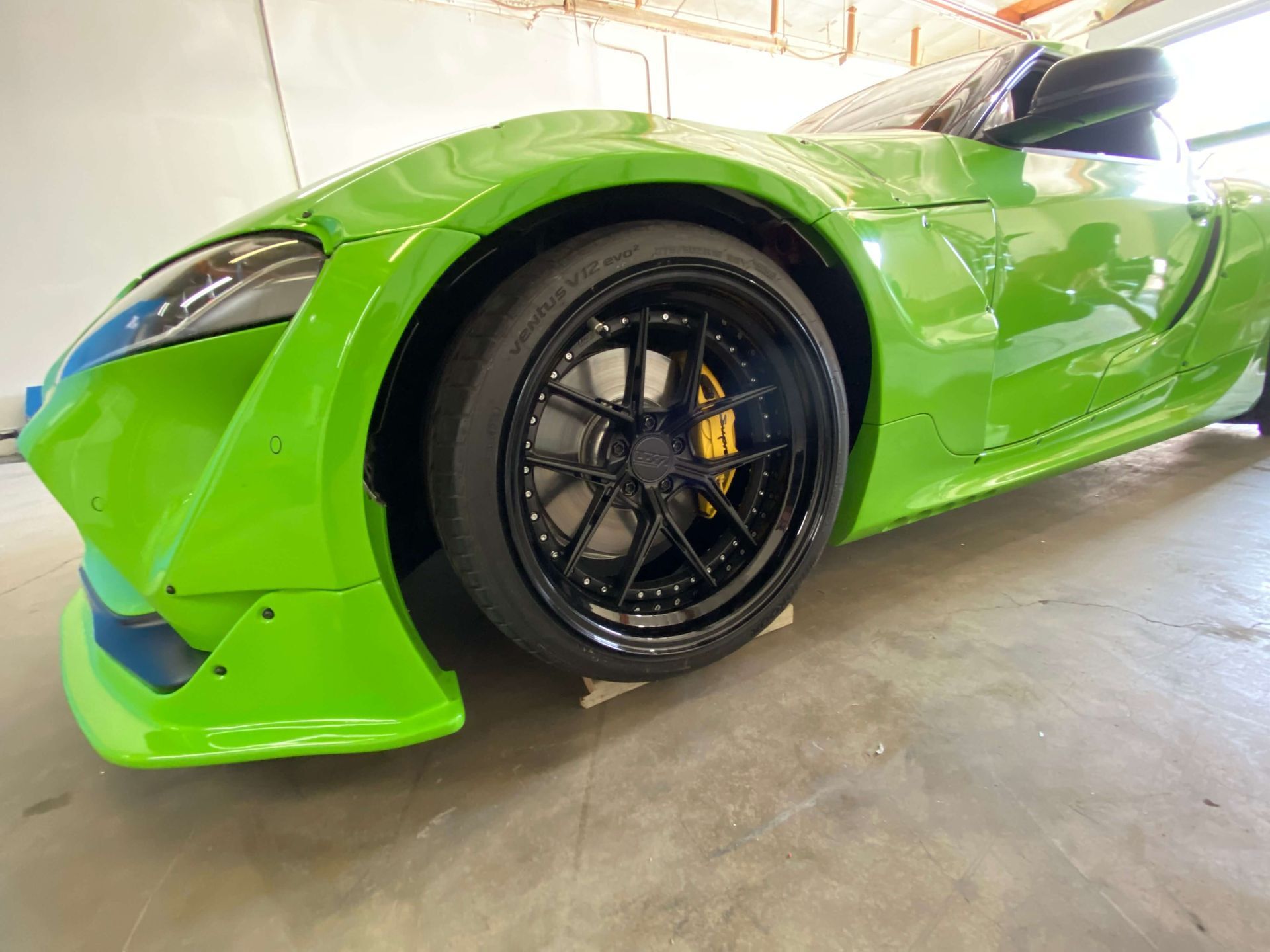 Bright green sports car front wheel and bumper in a garage